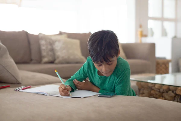 自宅で本にスケッチを描きながら携帯電話を使用するアメリカの少年の正面図 — ストック写真