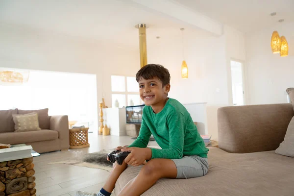 快適な家のリビングルームでソファでビデオゲームをプレイする幸せなアメリカの少年の側面図 — ストック写真