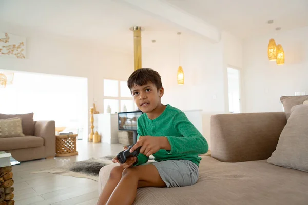 快適な家のリビングルームでソファでビデオゲームをプレイ愛らしいアメリカの少年の側面図 — ストック写真