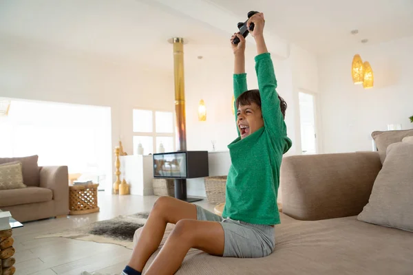快適な家のリビングルームでソファでビデオゲームをプレイ興奮したアメリカの少年の側面図 — ストック写真