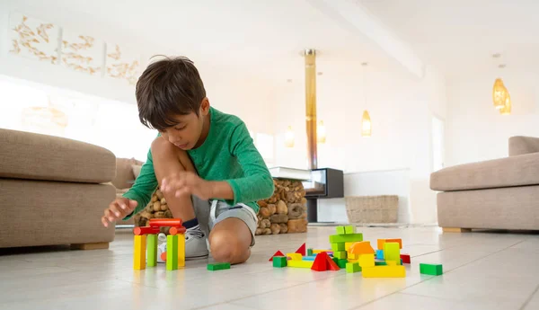 快適な家のリビングルームの床にビルディングブロックで遊ぶかわいいアメリカの少年の正面図 — ストック写真