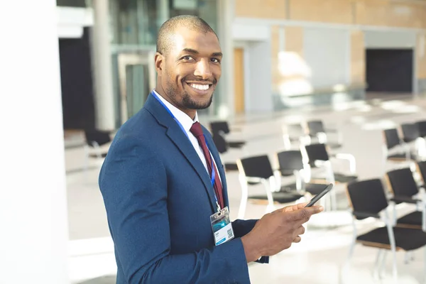 年轻的非洲裔美国男性高管站在空的会议室与手机 微笑对着相机的侧视图 — 图库照片