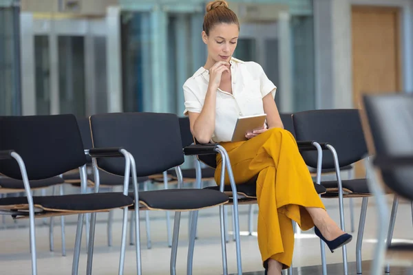 年轻的白种女性高管坐在空会议室的椅子上 看着数字平板电脑的前视图 — 图库照片