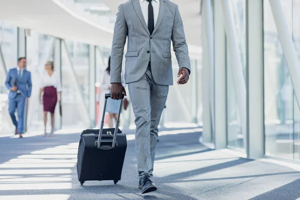 現代のオフィスでスーツケースを持って廊下を歩くアフリカ系アメリカ人ビジネスマンの低いセクション — ストック写真