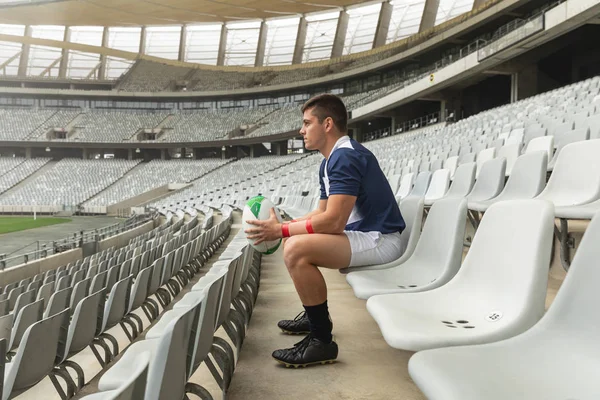 Düşünceli Beyaz Erkek Rugby Oyuncusu Stadyumda Ragbi Topuyla Oturuyor — Stok fotoğraf