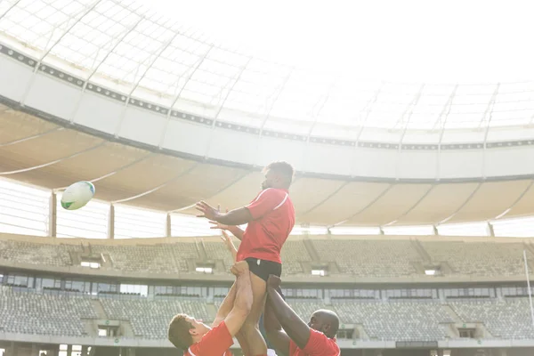 多様なラグビー選手が晴れた日にスタジアムで彼を保持しながら ボールをキャッチしようとしているアフリカ系アメリカ人の男性ラグビー選手の低角度側図 — ストック写真