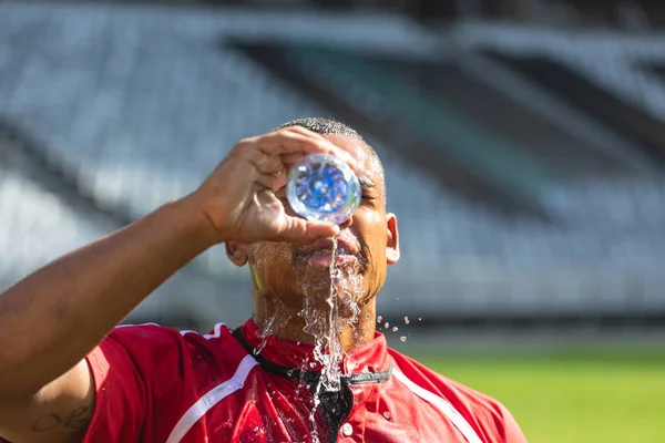 在阳光明媚的日子里 疲惫的非洲裔美国橄榄球运动员在体育场里把水瓶里的水倒在脸上的特写镜头 — 图库照片
