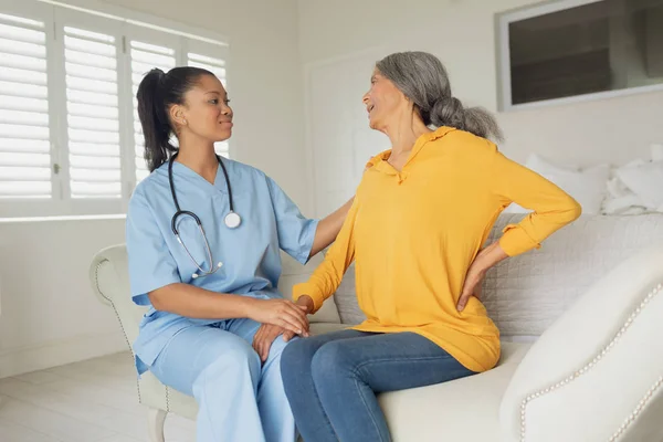 坐在室内沙发上的混合种族女医护人员和妇女的侧视图 正宗的退休老人生活理念 — 图库照片