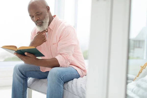 Vista Lateral Homem Afro Americano Lendo Livro Sentado Cama Quarto — Fotografia de Stock