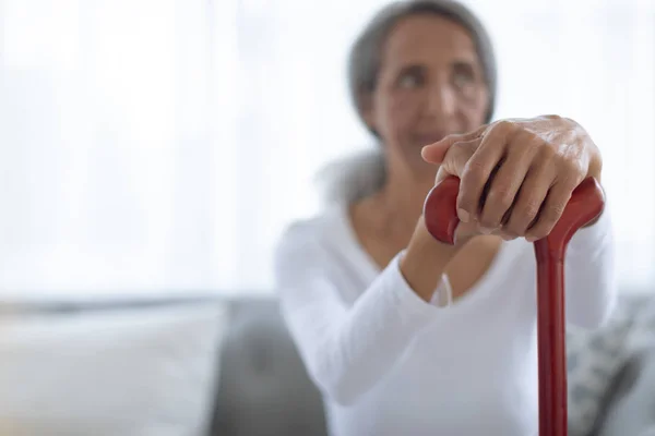 一边拿着棕色拐杖 一边坐在沙发上的资深混血女人的侧视图 正宗的退休老人生活理念 — 图库照片