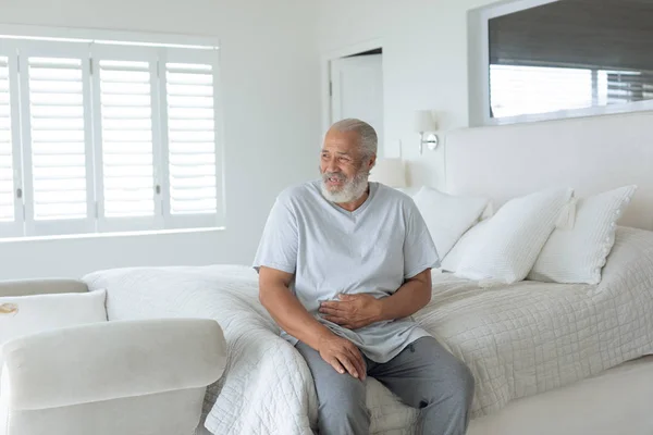寝室のベッドに座って微笑んで座っている先輩白人男性の側面図 本物のシニアリタイアライフコンセプト — ストック写真