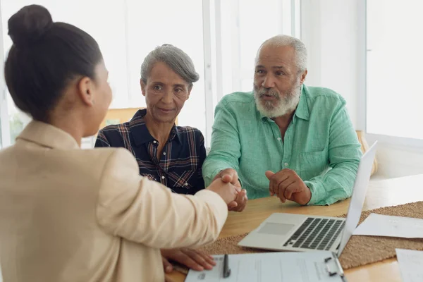 Side view of African-American man shaking hands with financial adviser while sitting beside wife indoor. Authentic Senior Retired Life Concept