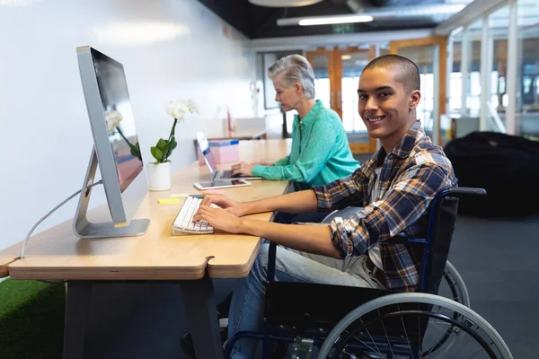 Side view of diverse executives working on computer and laptop at desk in office.