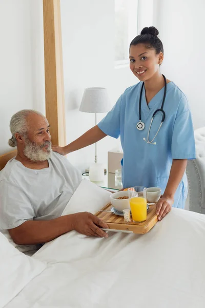 ベッドの中で老人を話す混合人種医療従事者の側面図 本物のシニアリタイアライフコンセプト — ストック写真