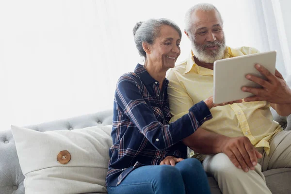 使用数字平板电脑时坐在沙发上的非洲裔美国夫妇的侧视图 正宗的退休老人生活理念 — 图库照片