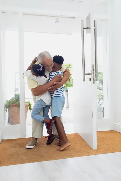 前视图的非洲裔美国人儿童拥抱他们的祖父在家里的大厅 正宗的退休老人生活理念 — 图库照片