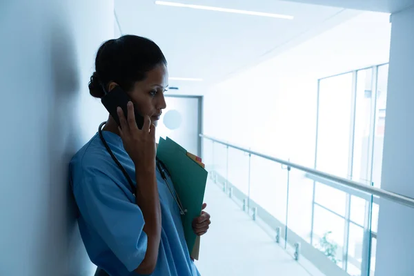 在医院走廊靠墙时 漂亮的混血女外科医生在手机上交谈的侧视图 — 图库照片