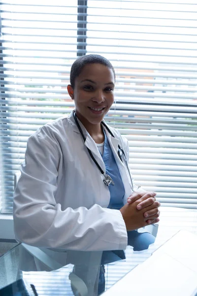 病院のカメラを見ながら手を握りしめながら座っている混合人種の女性医師の肖像画 — ストック写真