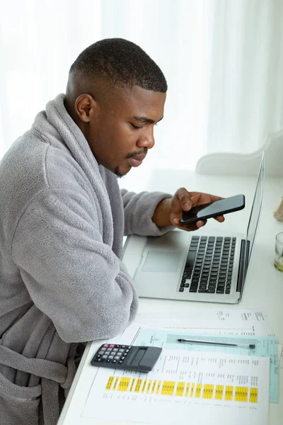 快適な家の寝室の机の上で携帯電話を使用しながら 紙幣を見ているアフリカ系アメリカ人の男性のサイドビュークローズアップ — ストック写真