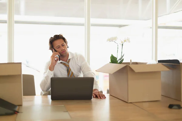 オフィスの会議室でラップトップを使用しながら携帯電話で話すハンサムな若い白人ビジネスマンの正面図 — ストック写真