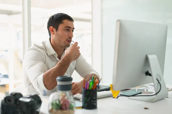 思慮深い若い白人男性グラフィックデザイナーの正面図オフィスの机でコンピュータを見て — ストック写真