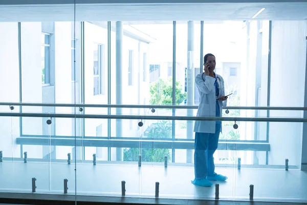 混合种族女外科医生在医院走廊用手机交谈的侧视图 — 图库照片