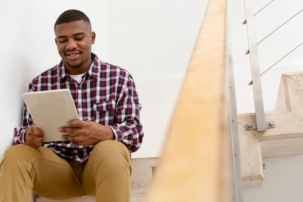 快適な家の階段に座っている間 デジタルタブレットを使用して幸せなアフリカ系アメリカ人の男性の正面図 — ストック写真