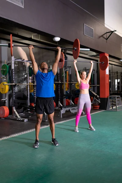 白人女性とアフリカ系アメリカ人男性がスポーツセンターの部屋の中で体重を持ち上げる正面図 — ストック写真