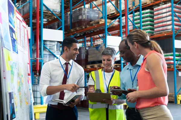 Front view of diverse warehouse staffs discussing over clipboard in warehouse