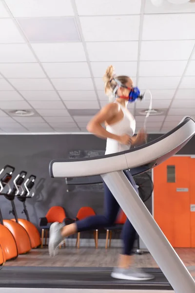 Side view of a Caucasian athletic woman doing a fitness test using a mask while using a treadmill inside a room at a sports center.
