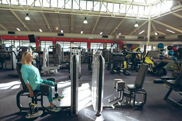 残疾人活跃的高级高加索妇女与截肢腿在健身工作室用腿卷曲机锻炼的侧视图 — 图库照片