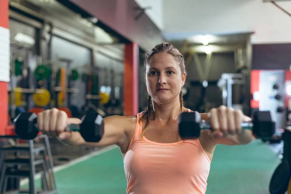 漂亮的年轻白人女运动员在健身室用哑铃锻炼的正面视图 — 图库照片