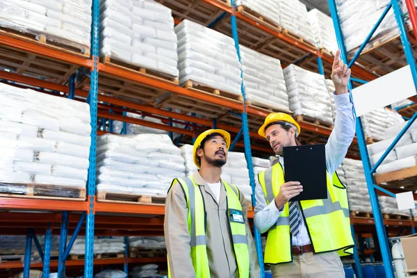 アジアの労働者と立って倉庫の距離を指すハンサムな白人男性監督の正面図 — ストック写真