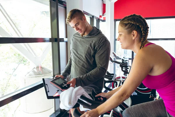 年轻的白种男性教练前视图协助年轻的高加索女运动员在健身工作室锻炼 — 图库照片
