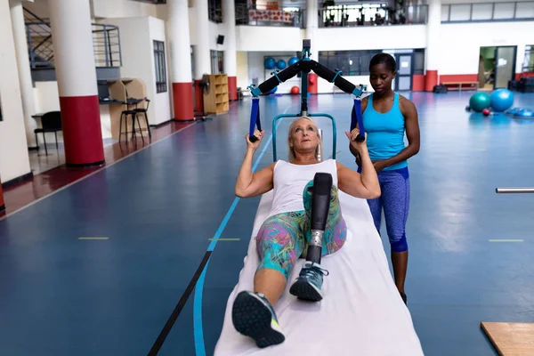 美籍非裔女教练员帮助白种人残疾老年妇女在体育中心锻炼的前瞻 — 图库照片