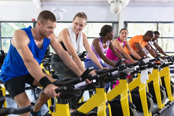 Side view of diverse fit people exercising on exercise bike in fitness center. Bright modern gym with fit healthy people working out and training at spin class