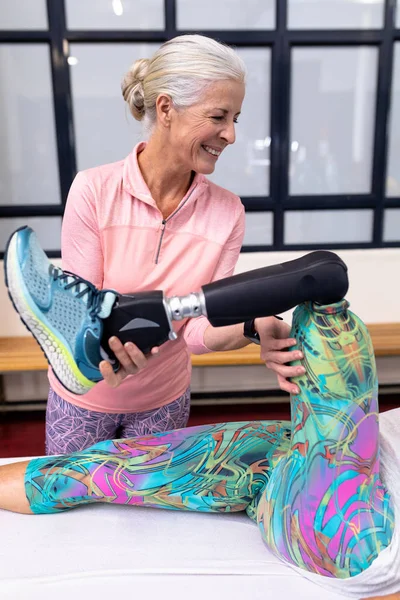 白种人快乐老年妇女在体育中心帮助白种人残疾妇女伸腿的前景 — 图库照片