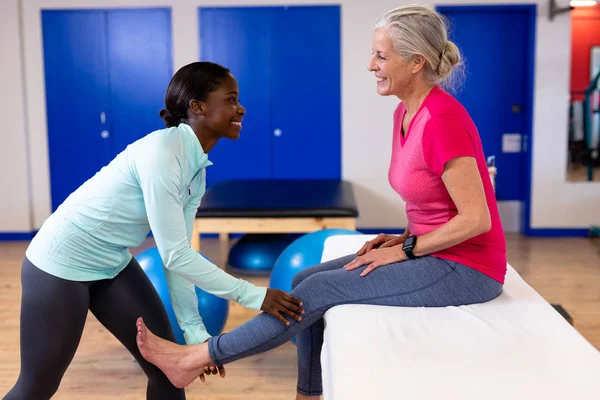 快乐的女性理疗师在体育中心为活跃的高级女性提供腿部按摩 — 图库照片