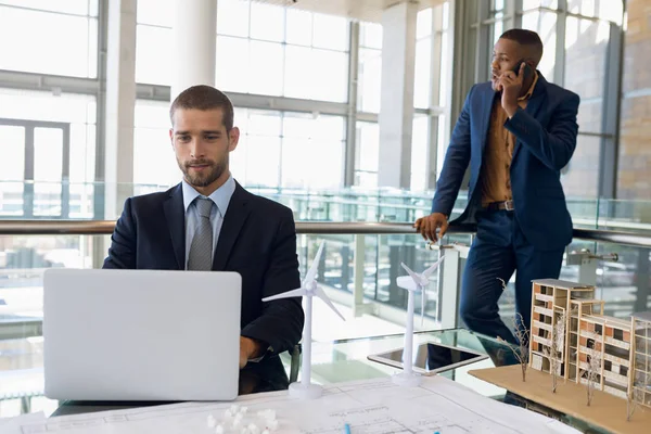 年轻的白种商人坐在建筑办公室的办公桌上使用笔记本电脑的正面视图 — 图库照片
