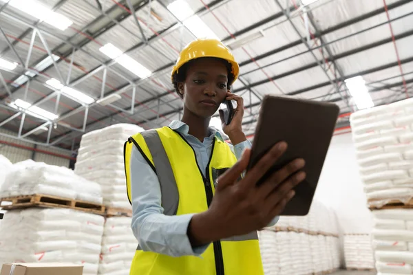 倉庫で携帯電話で話しながらデジタルタブレットを使用して女性労働者の低角度ビュー — ストック写真