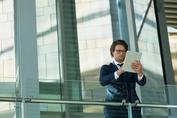 現代のオフィスの廊下で手すりに傾き デジタルタブレットを使用するビジネスマンの低角度ビュー — ストック写真