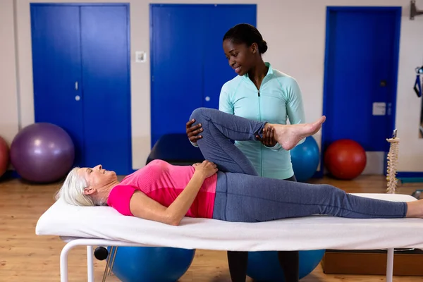 スポーツセンターでアクティブなシニア女性脚を伸ばす女性理学療法士 — ストック写真