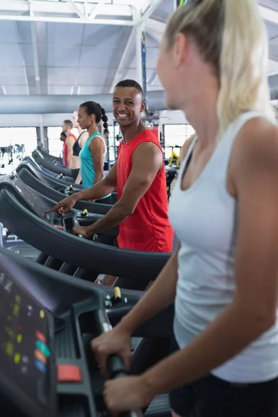健美黑人男子在健身中心跑步机上锻炼时与女人互动的侧视图 — 图库照片