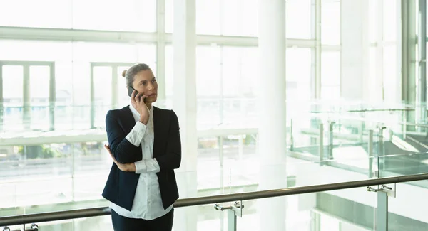近代的なオフィスビルの手すり付近で携帯電話で話すビジネスウーマンの正面図 — ストック写真