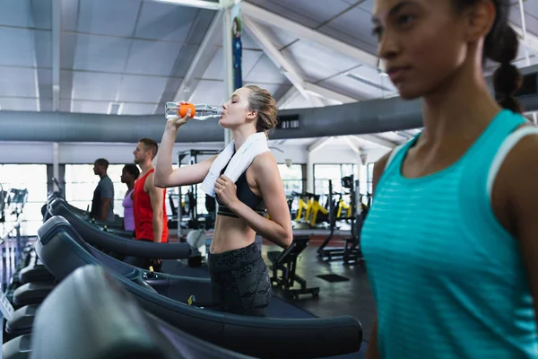 健身中心跑步机上运动时 白人健康妇女喝水的侧视图 — 图库照片