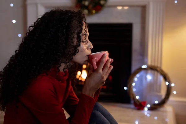 圣诞节时 一个混血女人坐在客厅的旁边 坐在壁炉旁 喝着杯子 — 图库照片