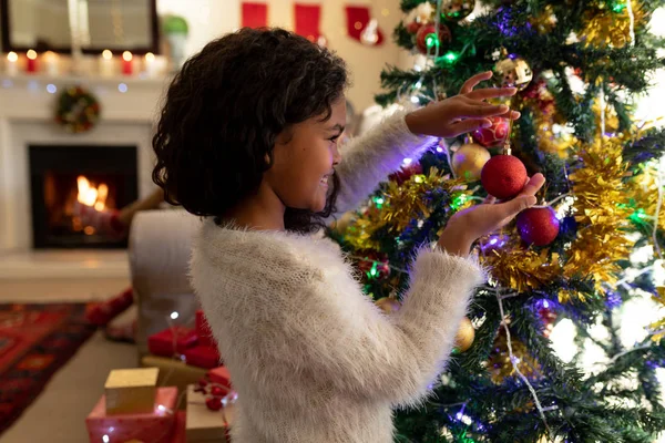 クリスマスに彼女の居間で若い混合レースの女の子の側面図 笑顔のクリスマスツリーを飾る — ストック写真