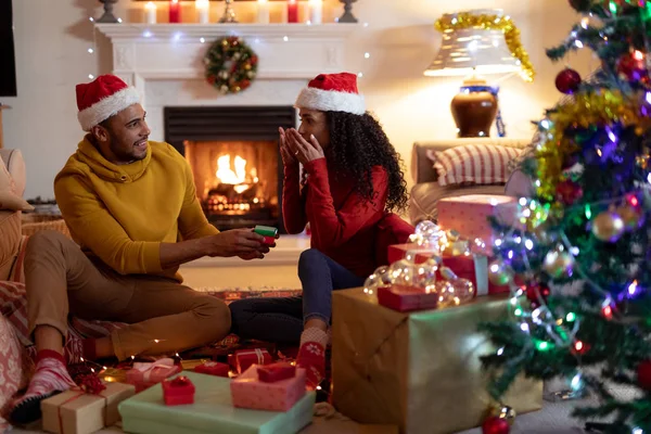 크리스마스에 자신의 거실에서 자신의 커플의 측면보기 바닥에 모자를 여자는 선물을주는 — 스톡 사진