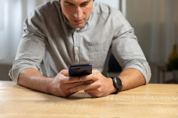 一个年轻的白种人男子坐在桌旁 在家里用智能手机的特写镜头 — 图库照片