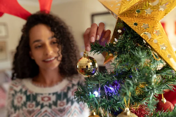 クリスマスに彼女の居間で混合レースの女性の正面図 お祝いの帽子を着て 笑顔とクリスマスツリーを飾る — ストック写真